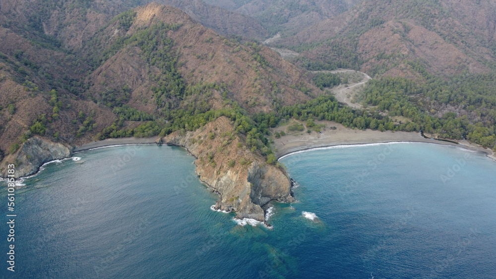 Two pebble beaches separated by a mountain with a mountain road leading to them with mountains on the background of the drone