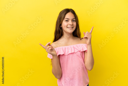 Little caucasian girl isolated on yellow background pointing finger to the laterals and happy