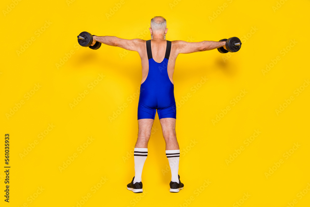 Full length photo back powerful professional powerlifting pensioner online coach showing spine dumbbells up isolated on yellow color background Full length photo back powerful professional powerlifting pensioner online coach showing spine dumbbells up isolated on yellow color background