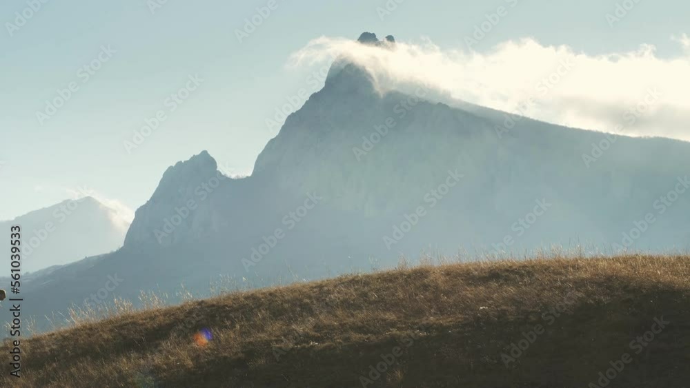 A runner strenuously runs along the top of the holna against the backdrop of a picturesque mountain. The person moves from left to right.