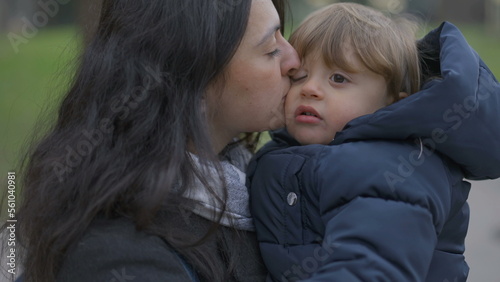 Mother walking outside holding baby toddler in arms, mom kissing son in cheek
