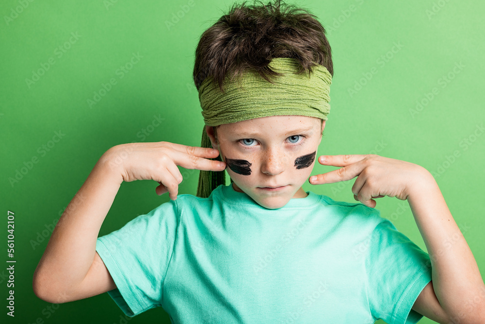 Boy drawing strips on cheeks against green background Boy drawing strips on cheeks against green background