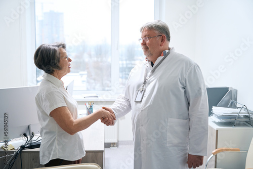 Doctor greets an elderly patient with handshake in medical office