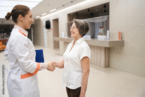 Young doctor greets an elderly patient in lobby of clinic