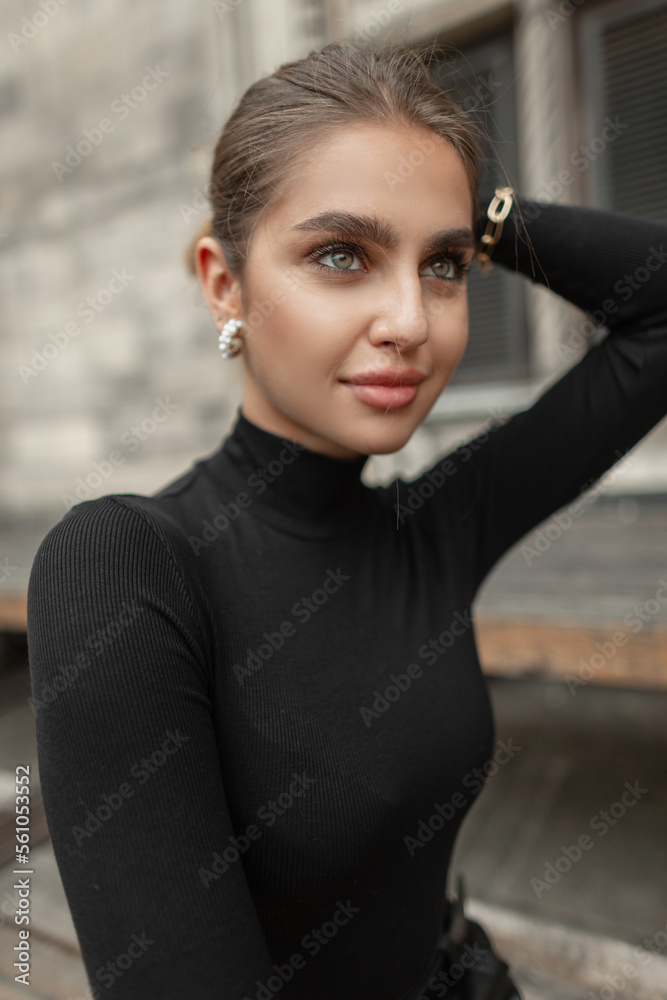 Close-up stylish female portrait of a trendy glamorous young beautiful girl with a clean face and beauty lips in fashion elegant black clothes with a long sleeve shirt in the city Close-up stylish female portrait of a trendy glamorous young beautiful girl with a clean face and beauty lips in fashion elegant black clothes with a long sleeve shirt in the city