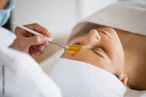 Crop cosmetologist with client during exfoliation procedure in spa salon
