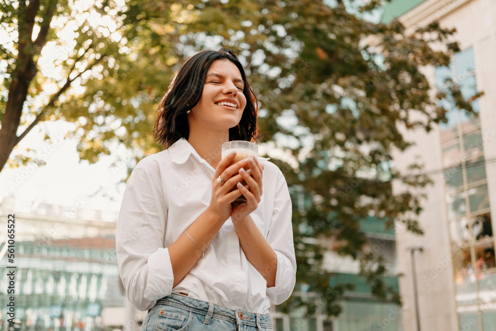 Young woman enjoys morning latte coffee from a glass outdoors in summer. Young woman enjoys morning latte coffee from a glass outdoors in summer.