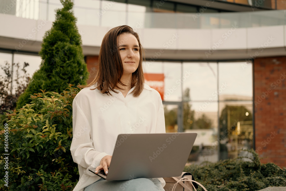 Dreamy woman is sitting outdoors holding a laptop while thinking about future. Dreamy woman is sitting outdoors holding a laptop while thinking about future.