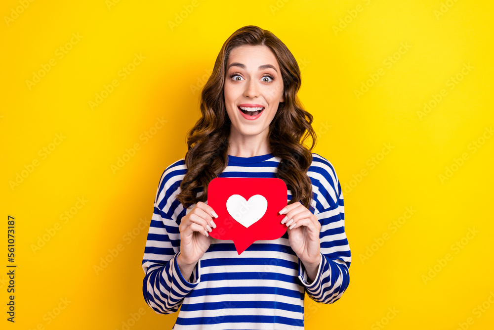 Photo of young excited funny astonised girl brown wavy hair surprised million red paper likes overjoyed isolated on yellow color background Photo of young excited funny astonised girl brown wavy hair surprised million red paper likes overjoyed isolated on yellow color background