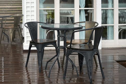 Wet tables with chairs outside the restaurant in the rain. There are puddles on the wooden floor. © ROMAN DZIUBALO