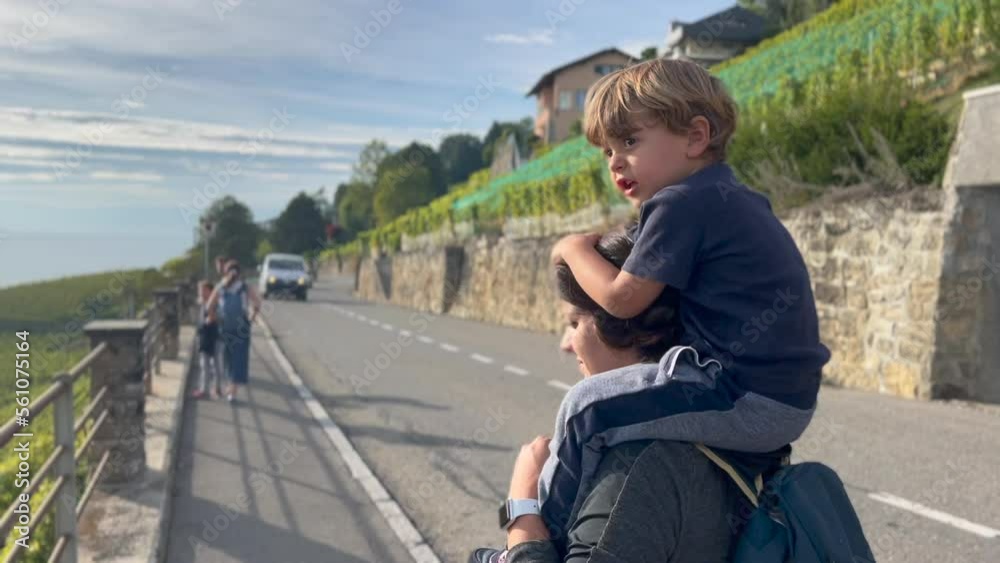 Back of little boy on mother shoulders walking outside in street traveling. Family on vacation Back of little boy on mother shoulders walking outside in street traveling. Family on vacation