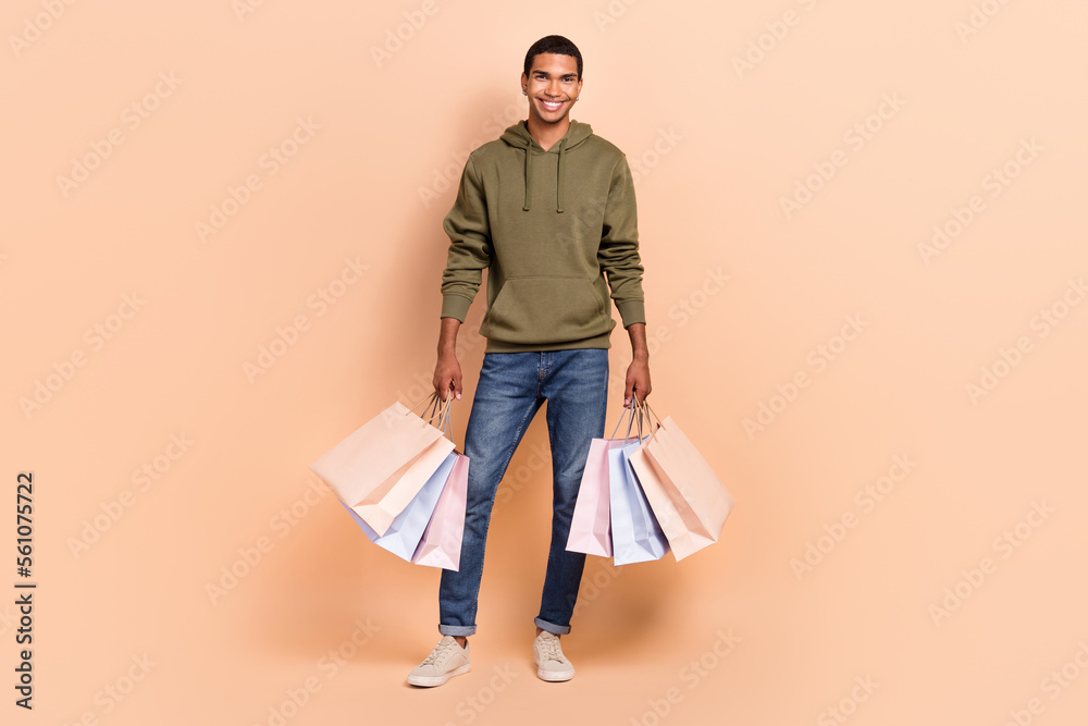 Full length photo of positive man wear khaki trendy clothes hands hold many packs nice shopping isolated on beige color background Full length photo of positive man wear khaki trendy clothes hands hold many packs nice shopping isolated on beige color background