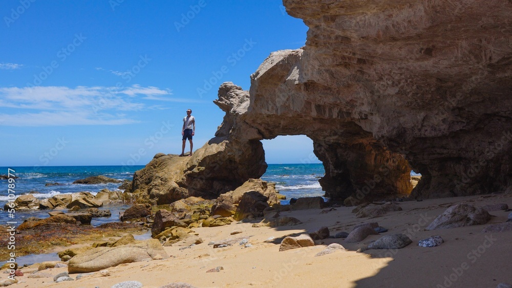 Man standing on rock arch in Cabo San Lucas, Mexico