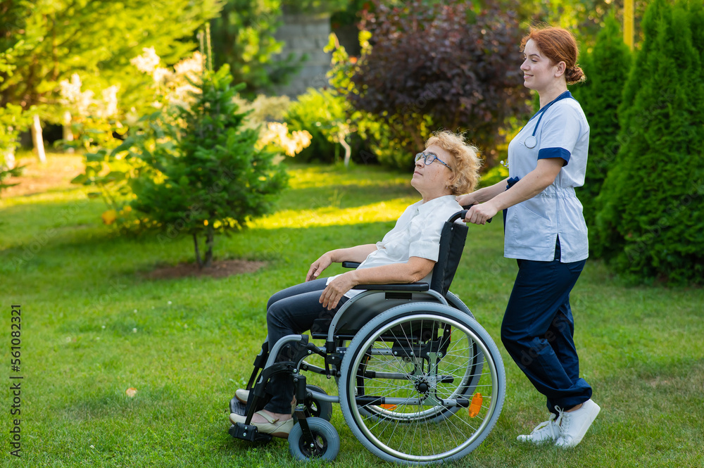 Caucasian female doctor walks with an elderly patient in a wheelchair in the park. Nurse accompanies an old woman on a walk outdoors. Caucasian female doctor walks with an elderly patient in a wheelchair in the park. Nurse accompanies an old woman on a walk outdoors.