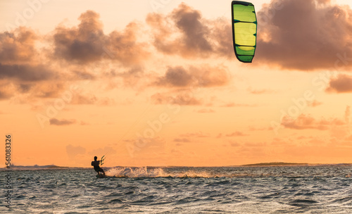 Sunset sky over the Indian Ocean bay with a kiteboarder riding kiteboard with a green bright power kite. Active sport people and beauty in Nature concept image. Le Morne beach, Mauritius.