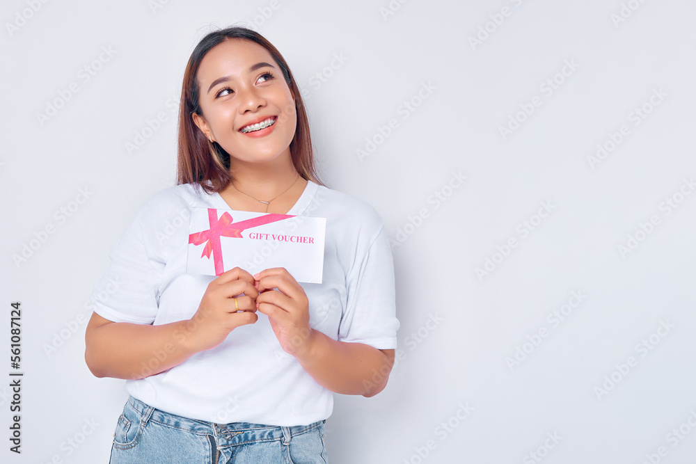 smiling young blonde woman girl Asian wearing casual white t-shirt holding gift certificate coupon voucher card and looking aside isolated on white background. People lifestyle concept smiling young blonde woman girl Asian wearing casual white t-shirt holding gift certificate coupon voucher card and looking aside isolated on white background. People lifestyle concept