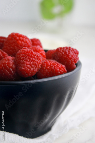 close up of fresh raspberries in dark bowl, blurred white background 