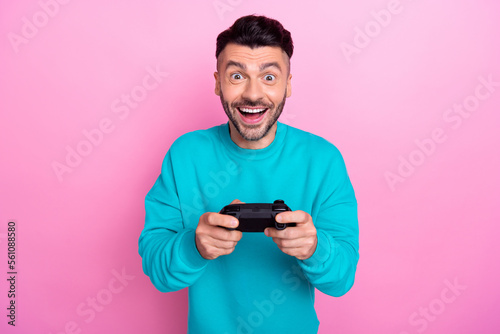 Photo of young addicted console gamer man student wear blue sweatshirt hold gamepad interested action isolated on pink color background © deagreez