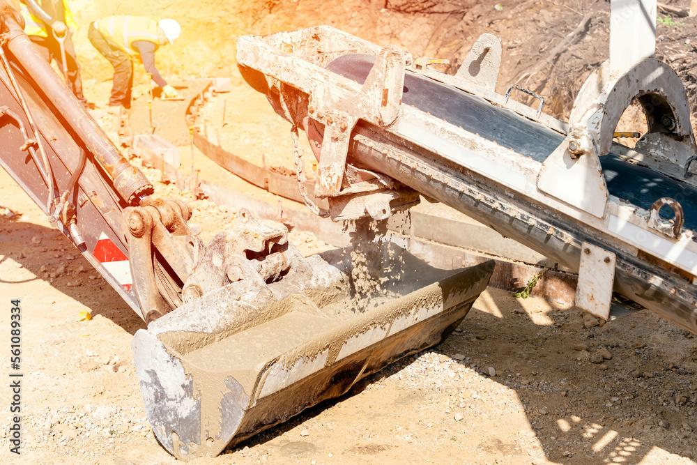 Concrete mixer truck pouring fresh wet concrete into excavators bucket at a construction site Concrete mixer truck pouring fresh wet concrete into excavators bucket at a construction site