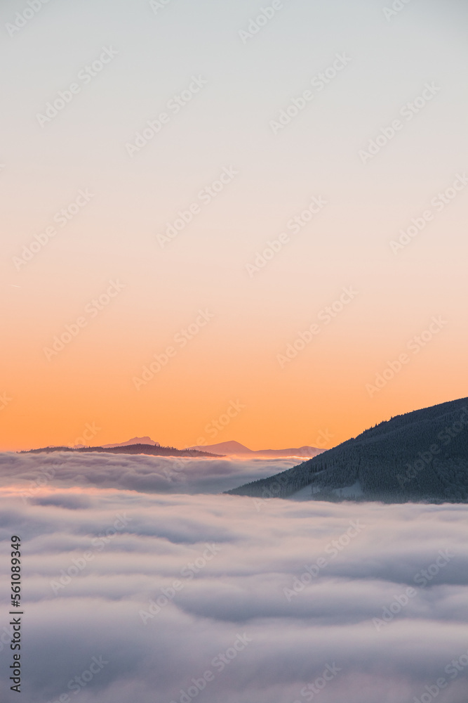 View of sea of clouds colored in the soft orange-pink hue of the morning sun. Peaks of the mountains rising out of this impermeable curtain. Sense of immortality and bliss. Beskydy, Czech republic