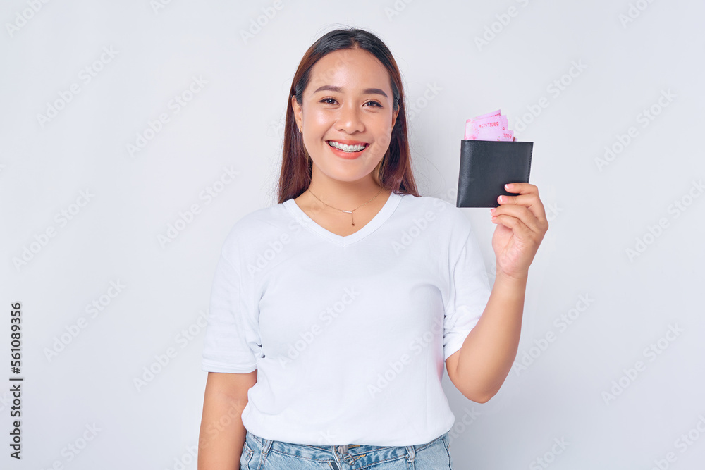 beautiful young woman girl Asian wearing casual white t-shirt and holding wallet full of money rupiah banknotes in hand, smiling at the camera isolated on white background. people lifestyle concept beautiful young woman girl Asian wearing casual white t-shirt and holding wallet full of money rupiah banknotes in hand, smiling at the camera isolated on white background. people lifestyle concept