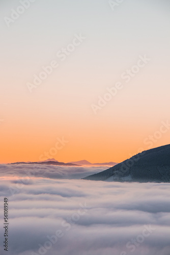 View of sea of clouds colored in the soft orange-pink hue of the morning sun. Peaks of the mountains rising out of this impermeable curtain. Sense of immortality and bliss. Beskydy, Czech republic