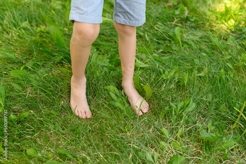 The child walks barefoot on the green grass. The effect of massage on the nerve endings of the legs is the prevention of flat feet in children. The concept of hardening, meditation.