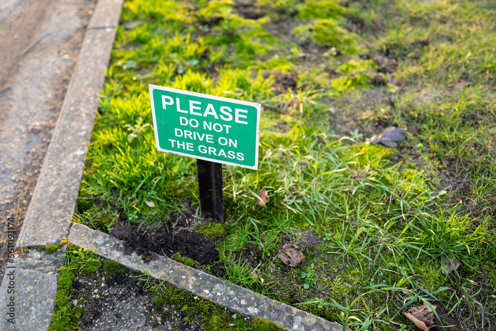 Shallow focus of a small and polite No Parking sign seen on a grass verge outside a private house.
