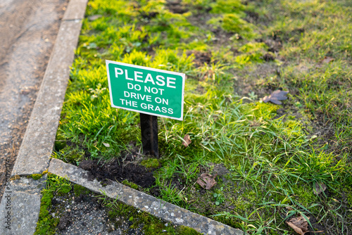 Shallow focus of a small and polite No Parking sign seen on a grass verge outside a private house.