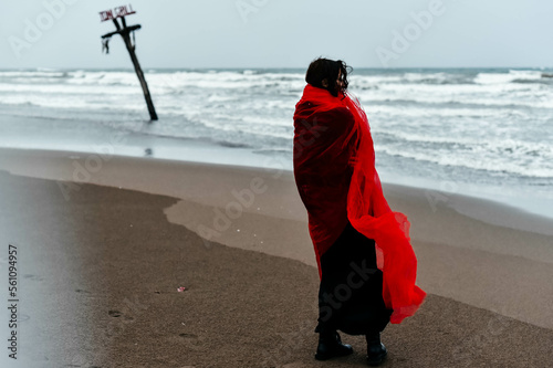 Silhouette woman in black dress with red scarf walking on the winter beach