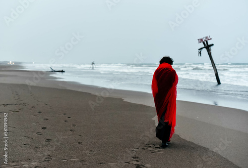 Silhouette woman in black dress with red scarf walking on the winter beach