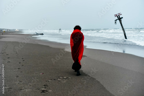 Silhouette woman in black dress with red scarf walking on the winter beach