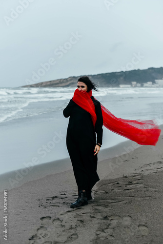 Portrait woman in black dress walking with red scarf on the winter beach