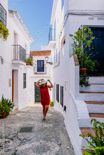 Woman walking with a hat in a street of traditional spanish village Frigiliana, solo female travel concept photo