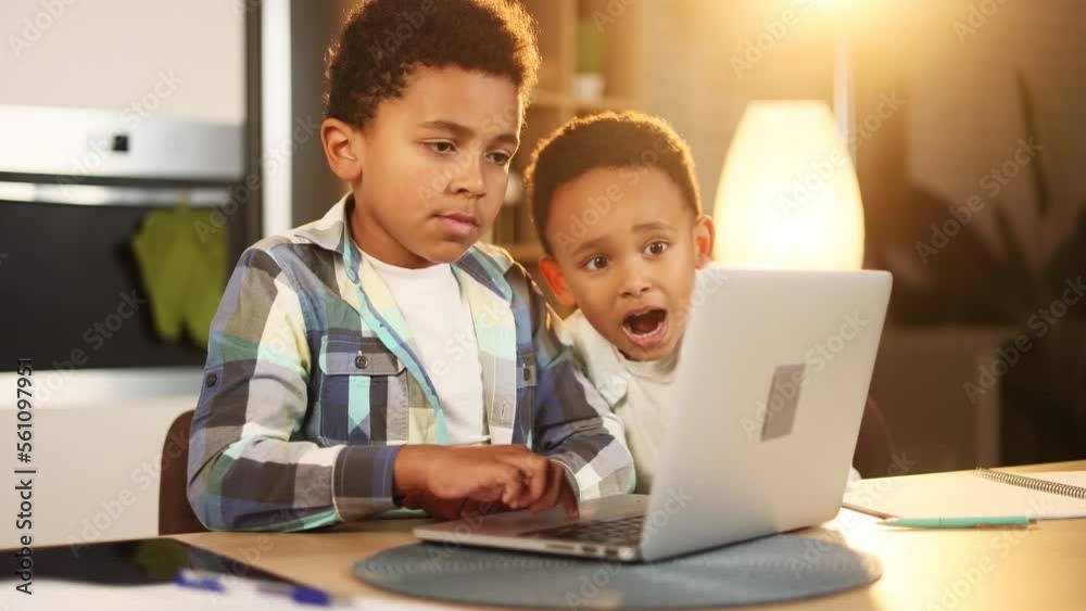 Cute little boys brothers using laptop computer browsing web learning reading online social media content looking for toys in internet store at home kitchen Technology children addiction concept Cute little boys brothers using laptop computer browsing web learning reading online social media content looking for toys in internet store at home kitchen Technology children addiction concept