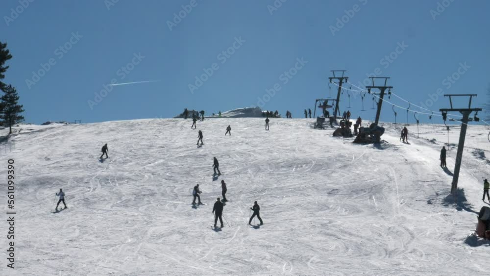 Silhouettes of people skiing downhill in a mountain ski resort. Clear blue sky in the background. Sunny winter day Silhouettes of people skiing downhill in a mountain ski resort. Clear blue sky in the background. Sunny winter day