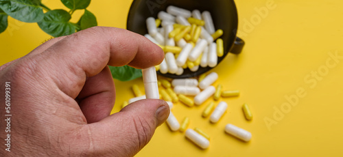 Fingers holding a medicine capsule on a yellow background