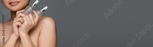cropped view of woman with perfect skin holding bottles of rejuvenating cosmetic serum isolated on grey, banner.