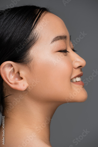 Side view of smiling asian woman closing eyes isolated on grey.