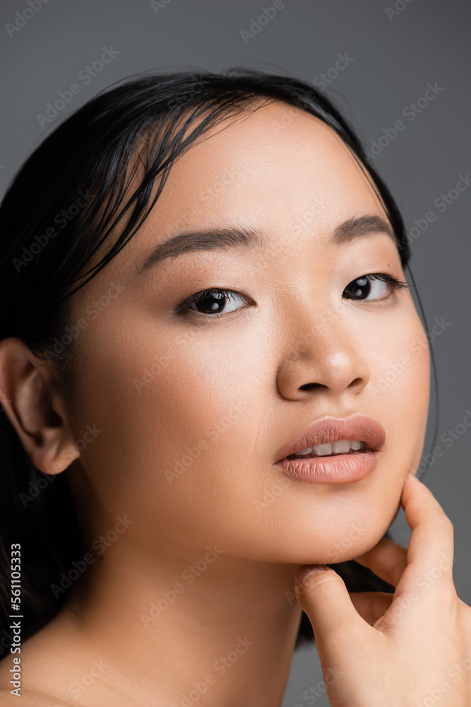 portrait of brunette asian woman with nude makeup looking at camera isolated on grey. portrait of brunette asian woman with nude makeup looking at camera isolated on grey.