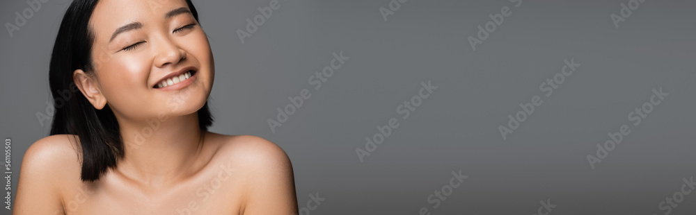 young asian woman with bare shoulders and perfect skin smiling with closed eyes isolated on grey, banner. young asian woman with bare shoulders and perfect skin smiling with closed eyes isolated on grey, banner.