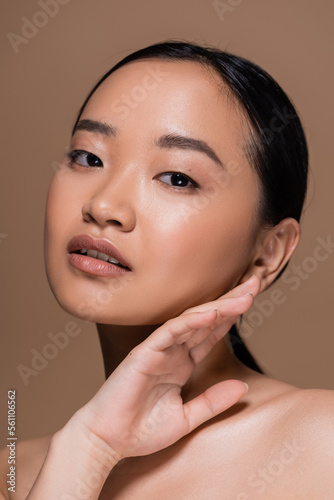Portrait of young asian woman touching face isolated on brown.
