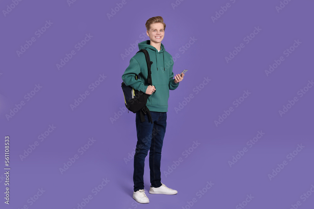 Teenage boy with backpack using smartphone on purple background Teenage boy with backpack using smartphone on purple background