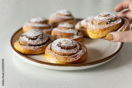 Freshly baked cinnamon rolls sprinkled with powdered sugar on parchment paper. Sweet homemade Christmas baking. . Kanelbule is a Swedish dessert.