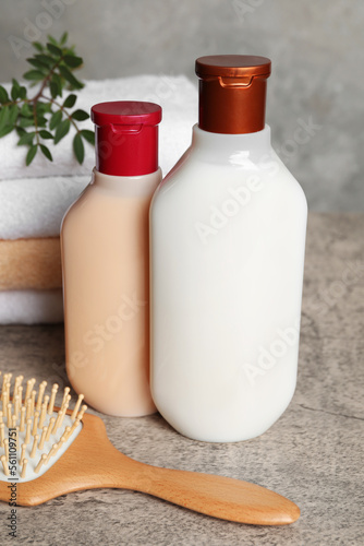 Bottles of shampoo, hairbrush and stacked towels on grey table, closeup