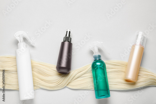 Spray bottles with thermal protection and lock of blonde hair on light background, flat lay