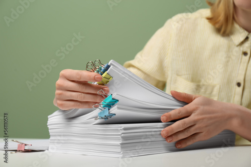 Woman stacking documents at white table against green background, closeup