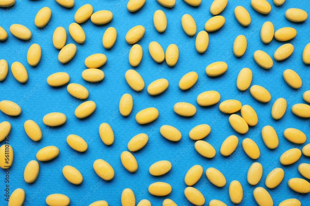 Many yellow dragee candies on blue background, flat lay