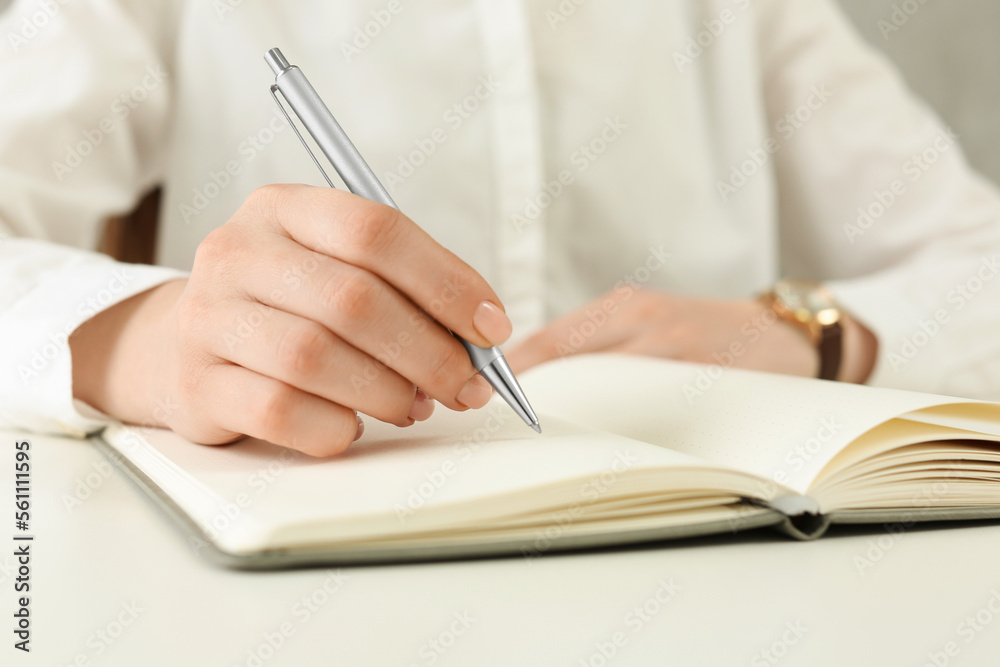 Woman writing in notebook at white table, closeup - obrazy, fototapety, plakaty 