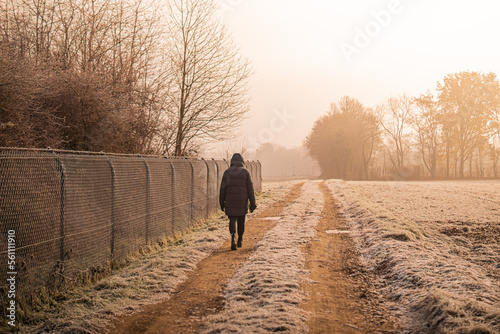 A young woman walks along a country road covered with frost in winter © just.kev